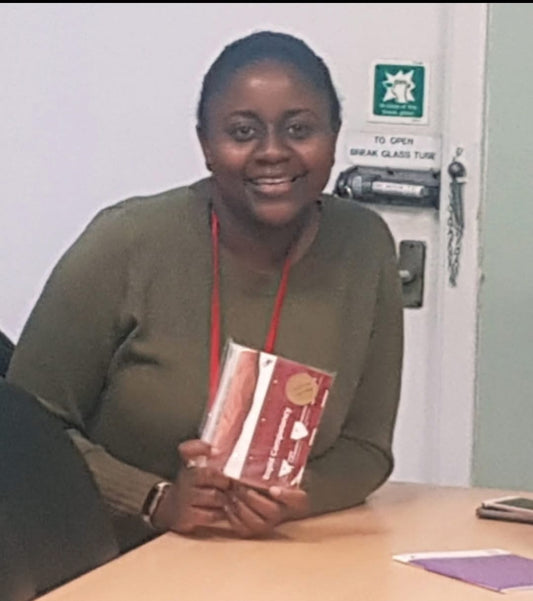 Woman holding a book in an indoor setting with a whiteboard and door in the background.VeinTrain flat-pack vein simulator for phlebotomy and cannulation training
